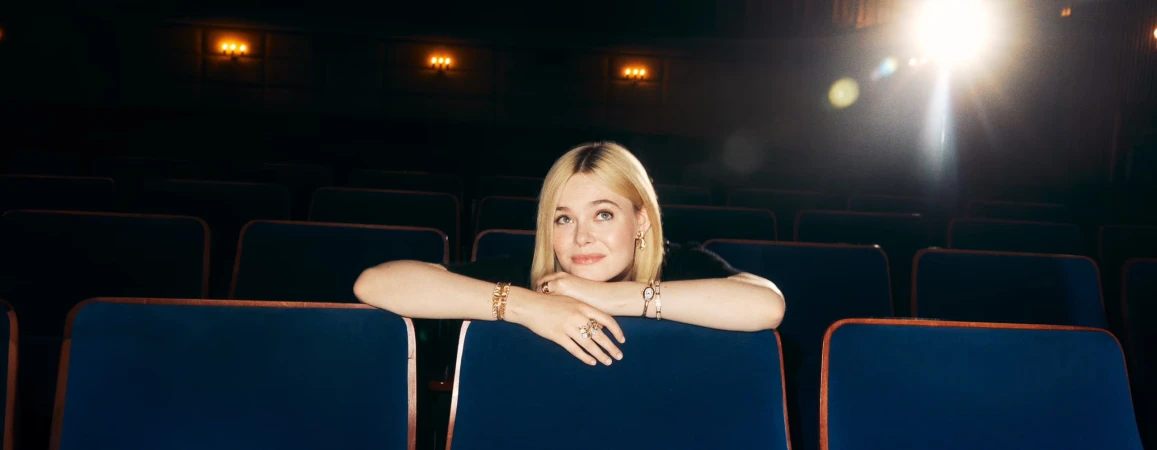 Elle Fanning leaning on theater seats wearing gold jewelry in a cinema for Cartier Fall 2024 ad campaign