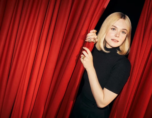 Elle Fanning wearing statement rings and a black top parting heavy red curtains in a campaign image for Cartier.