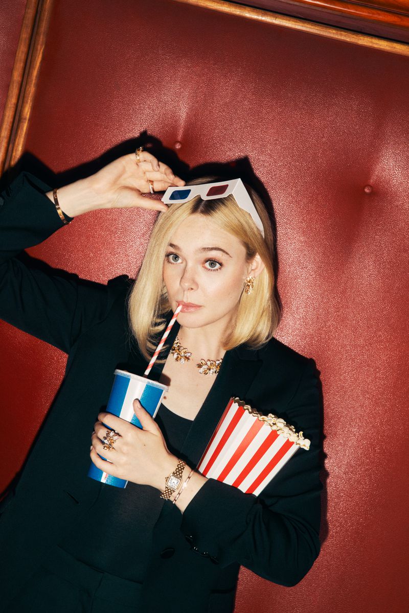 Elle Fanning wearing black blazer and gold jewellery holding popcorn and drink with 3D glasses on her head