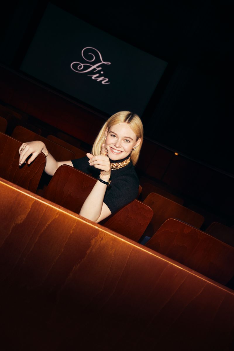 Elle Fanning smiling in a movie theatre seat pointing forward for Cartier Fall 2024 ad campaign