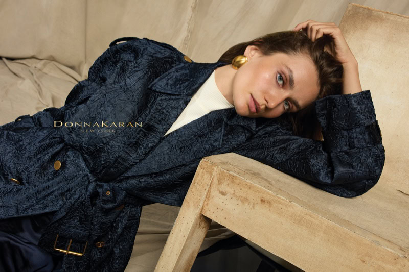 Model Andreea Diaconu in a dark blue textured coat leaning against a wooden block in a campaign shot by Alique for Donna Karan.