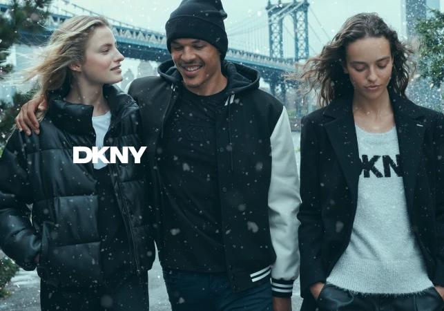 Three models walking outdoors in winter wearing DKNY outerwear with a suspension bridge visible in the background.