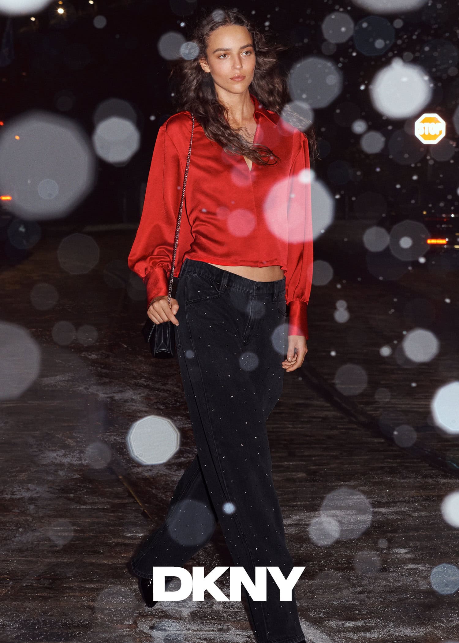 Model in red satin blouse and dark jeans walking outdoors at night with bokeh light effects for DKNY