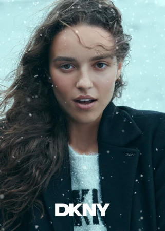 Close-up portrait of a woman wearing a dark coat and fuzzy white sweater amidst falling snow, for DKNY.