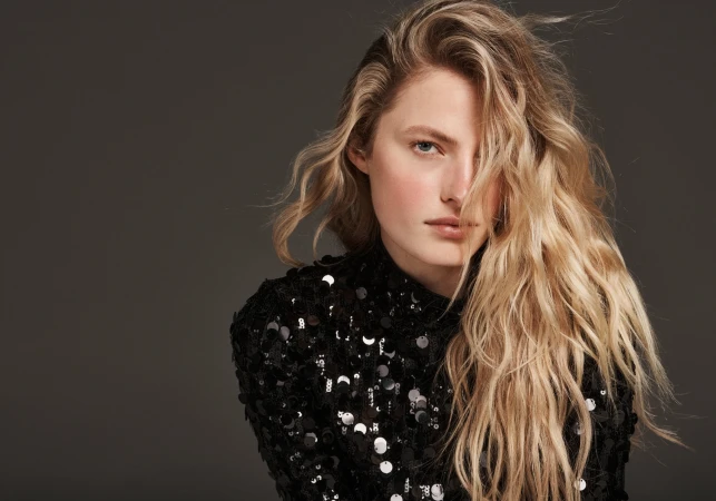 Portrait of a blonde model wearing a black sequined top against a dark grey seamless studio backdrop