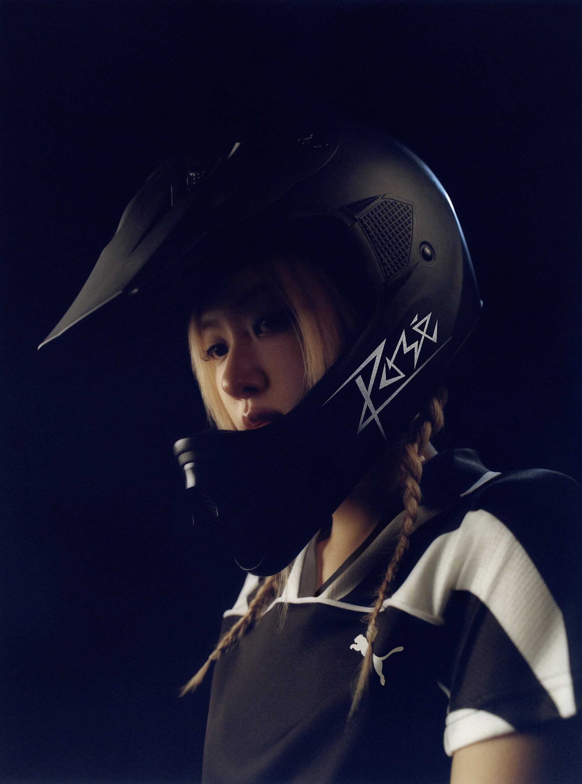 Close-up portrait of Rosé Park wearing a black helmet and black and white Puma athletic jersey against a dark background.