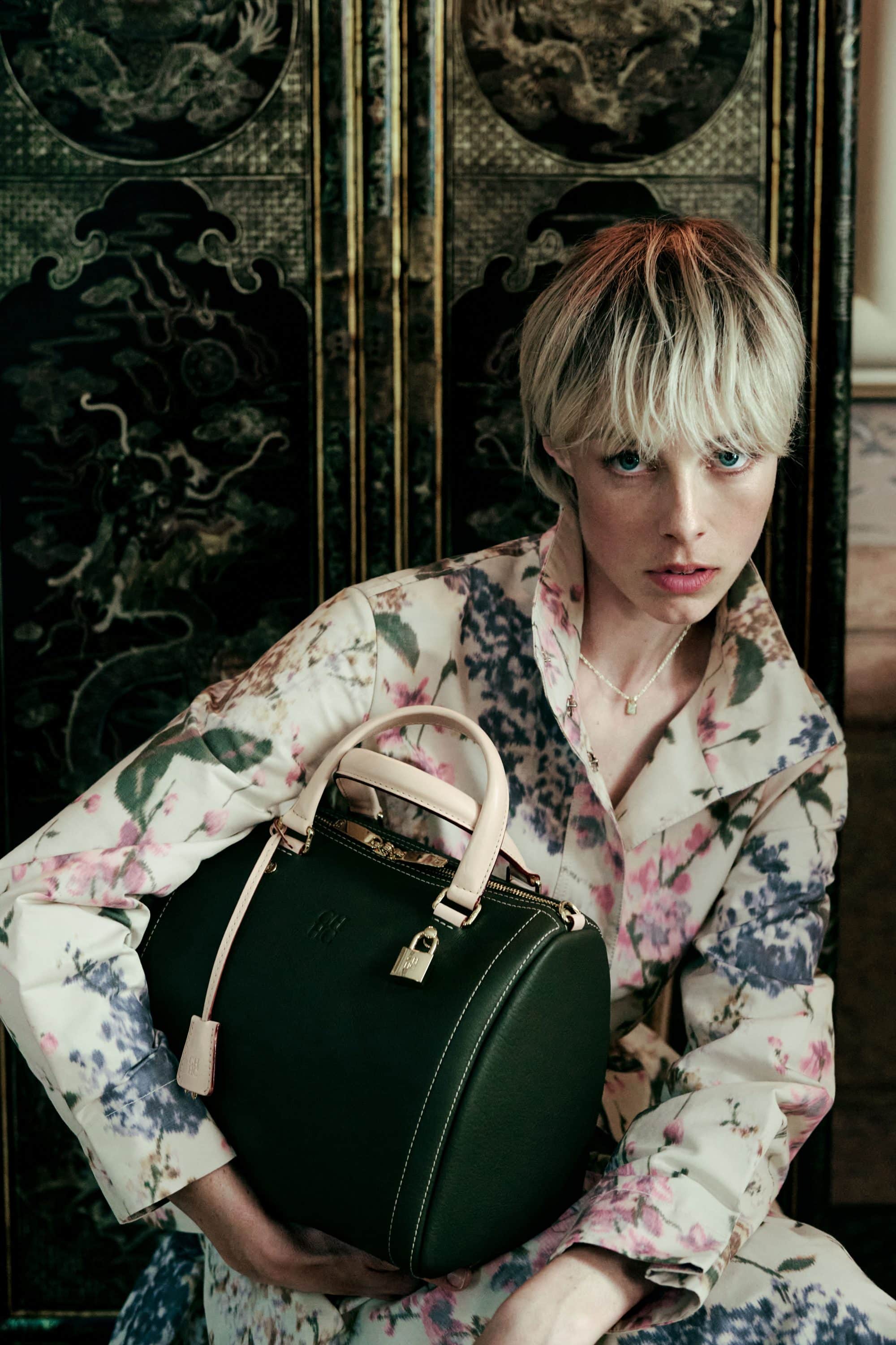 Model Edie Campbell holding a dark green leather handbag, wearing a floral patterned coat for CH Carolina Herrera.
