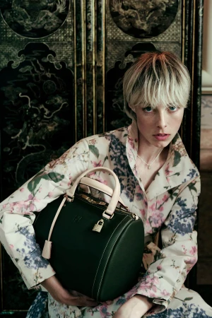 Model Edie Campbell holding a dark green leather handbag, wearing a floral patterned coat for CH Carolina Herrera.