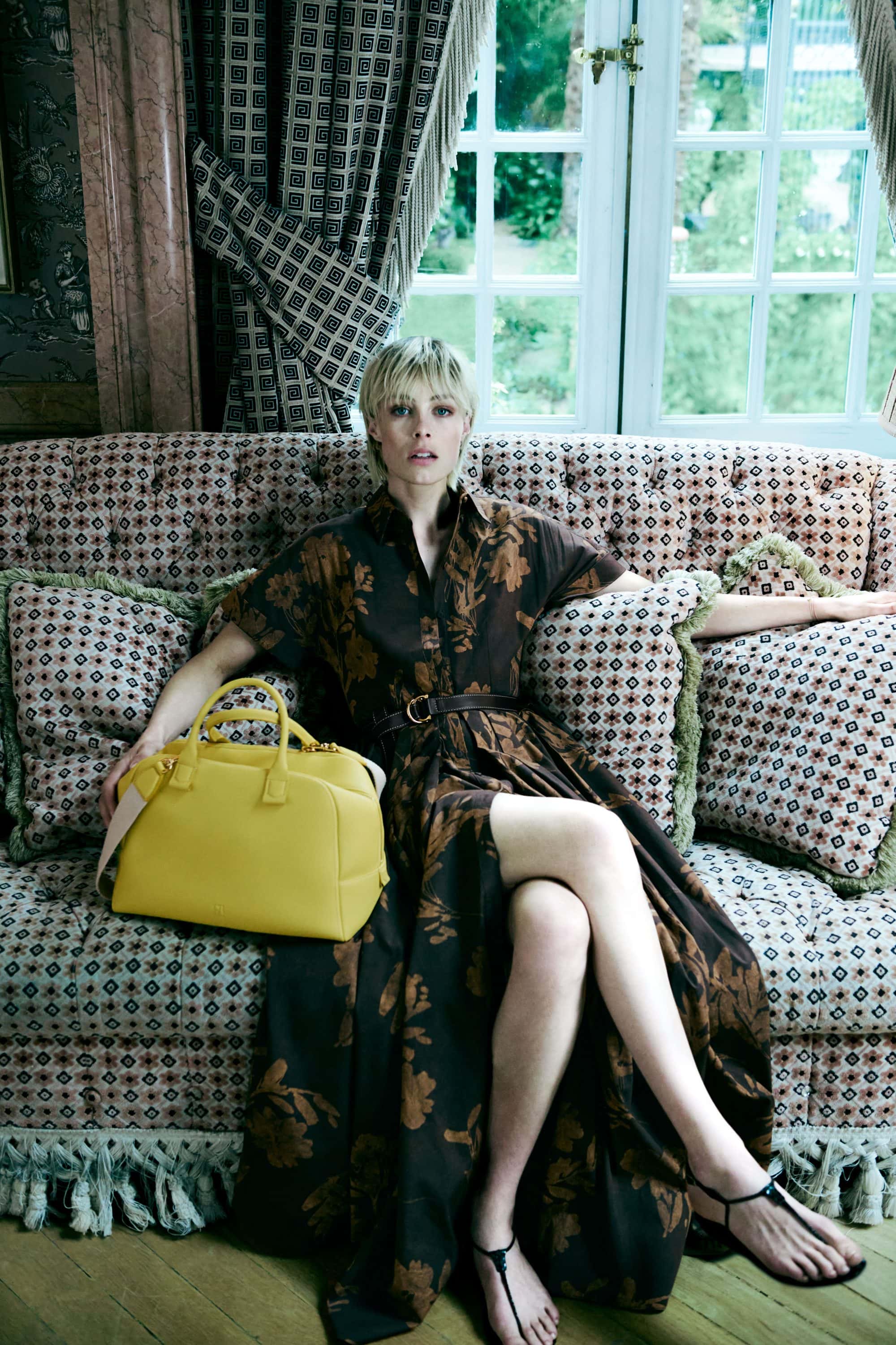 Model Edie Campbell seated on a patterned sofa holding a bright yellow handbag for CH Carolina Herrera ad campaign.