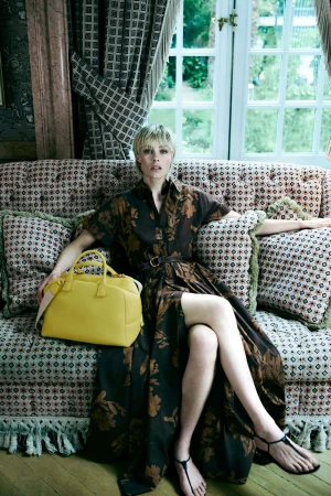 Model Edie Campbell seated on a patterned sofa holding a bright yellow handbag for CH Carolina Herrera ad campaign.