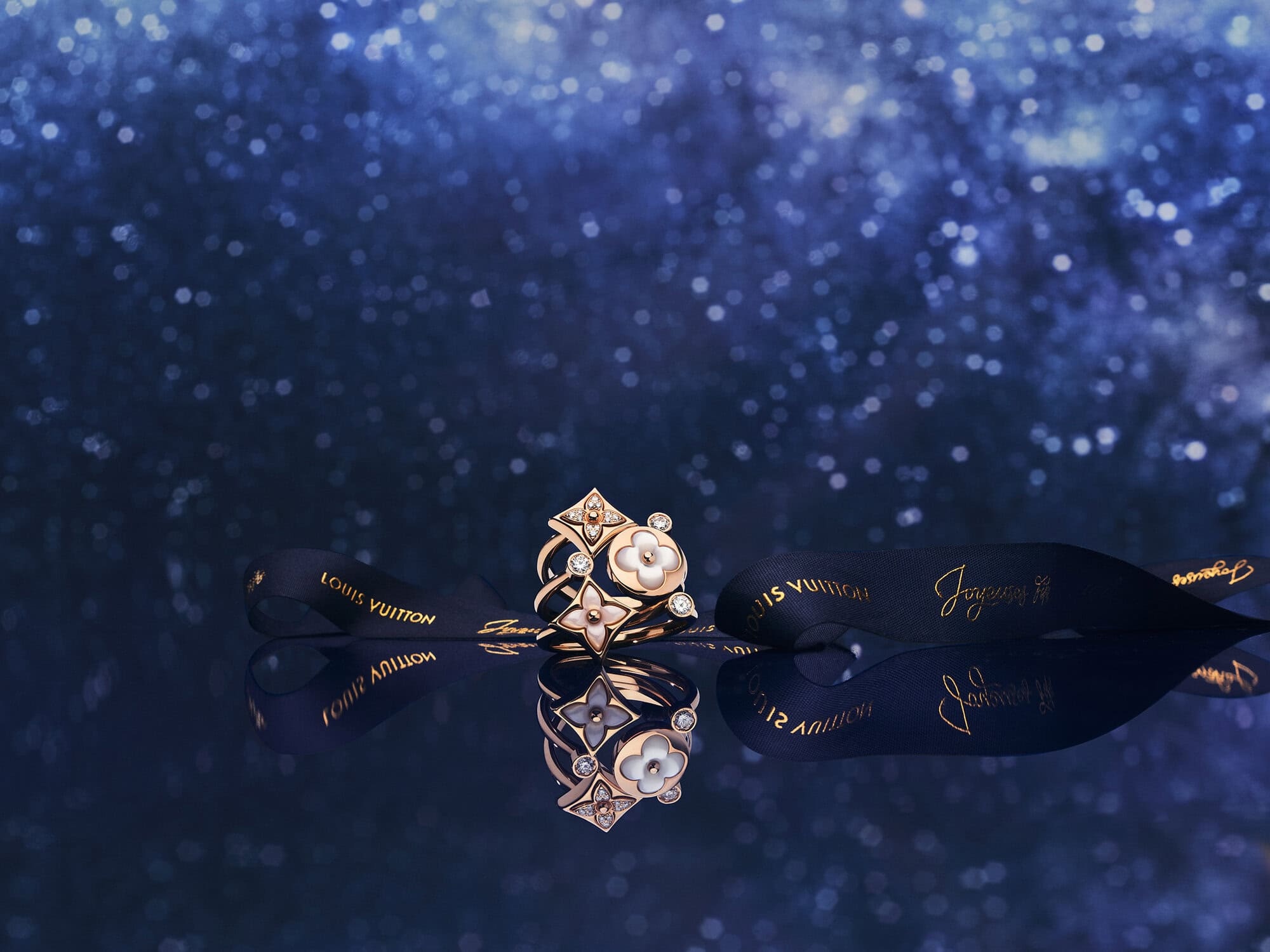 Louis Vuitton ring and dark ribbon reflecting on a glossy surface against a starry blue background
