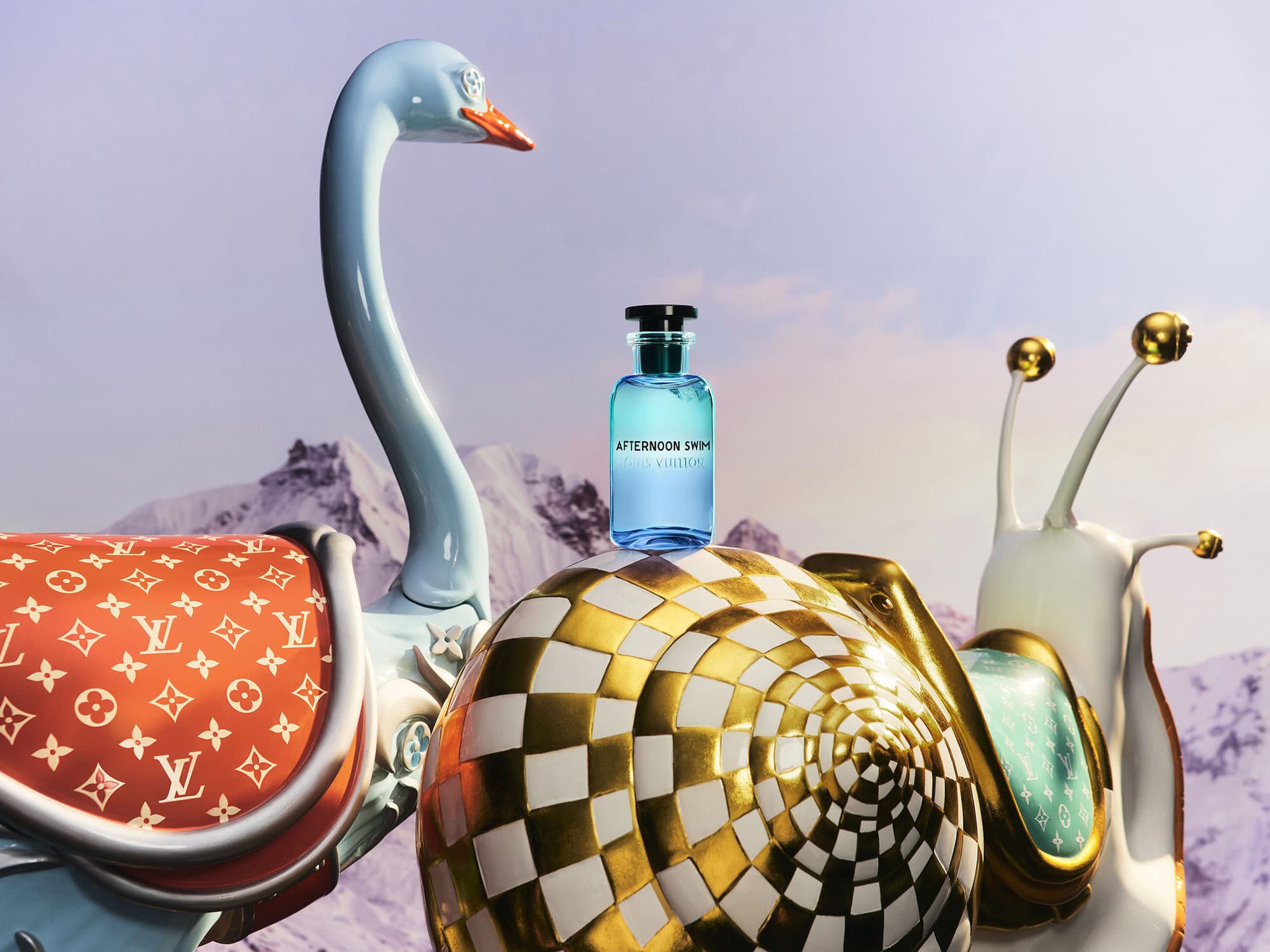 Blue perfume bottle resting on a gold and white snail sculpture next to a blue bird sculpture against a mountain landscape background