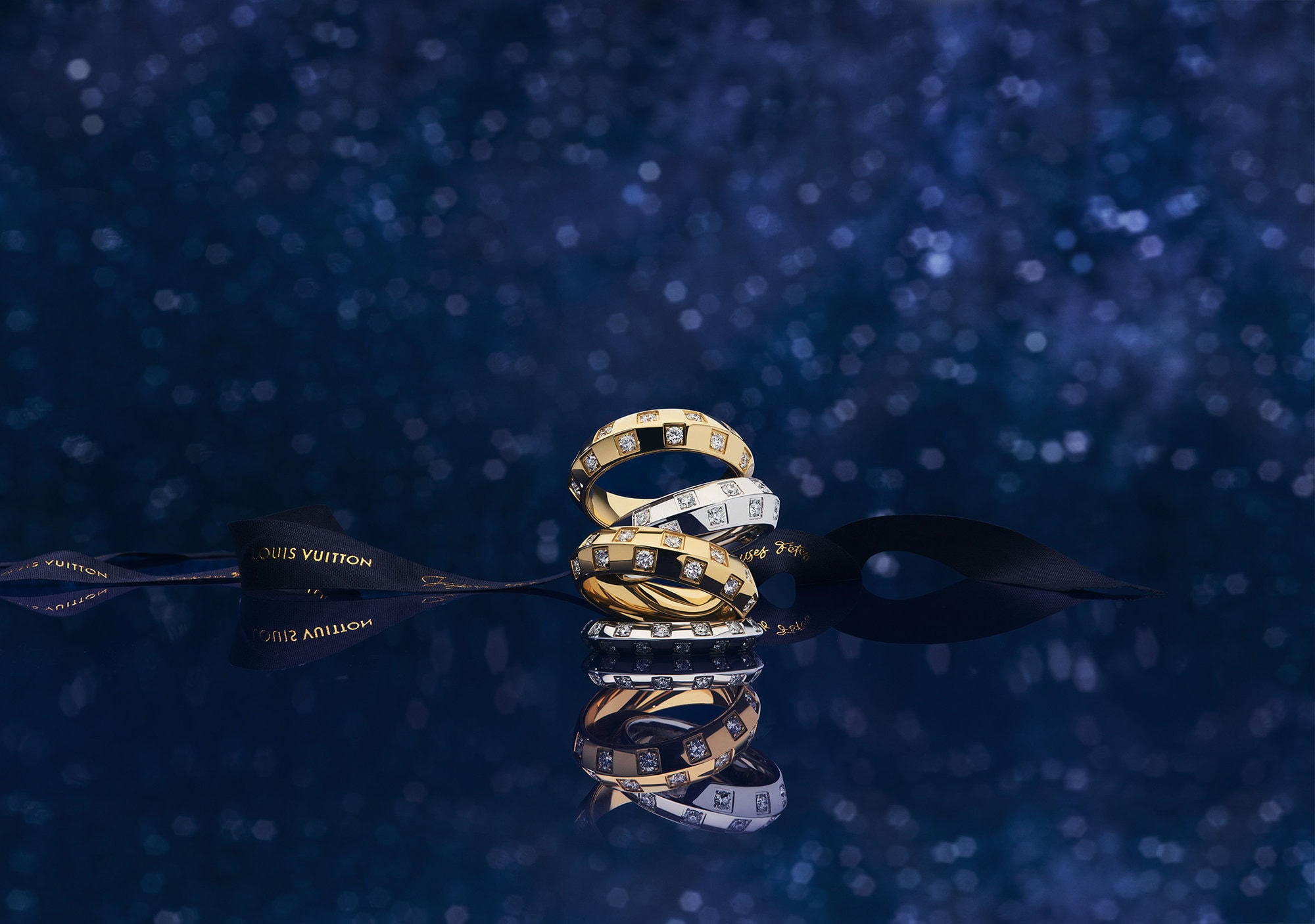 Stacked diamond rings and a black ribbon on a reflective dark blue sparkling background