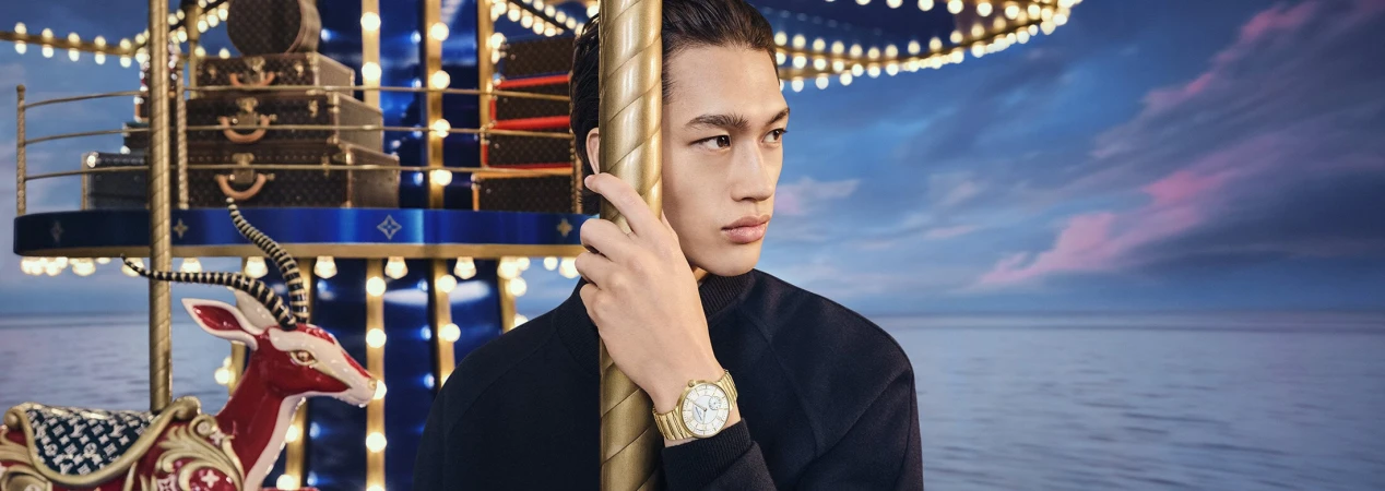 Young man holding a carousel pole wearing a dark jacket with a gold watch against a carousel and sunset sky