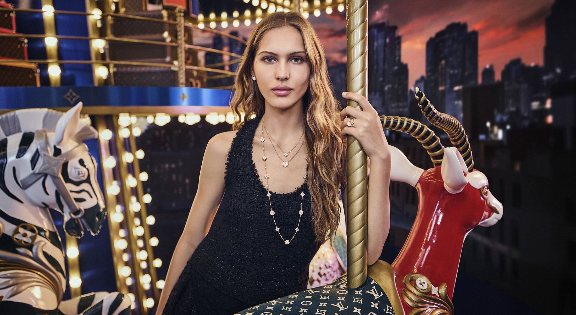Model standing on a carousel holding a golden pole wearing layered necklaces and a black top