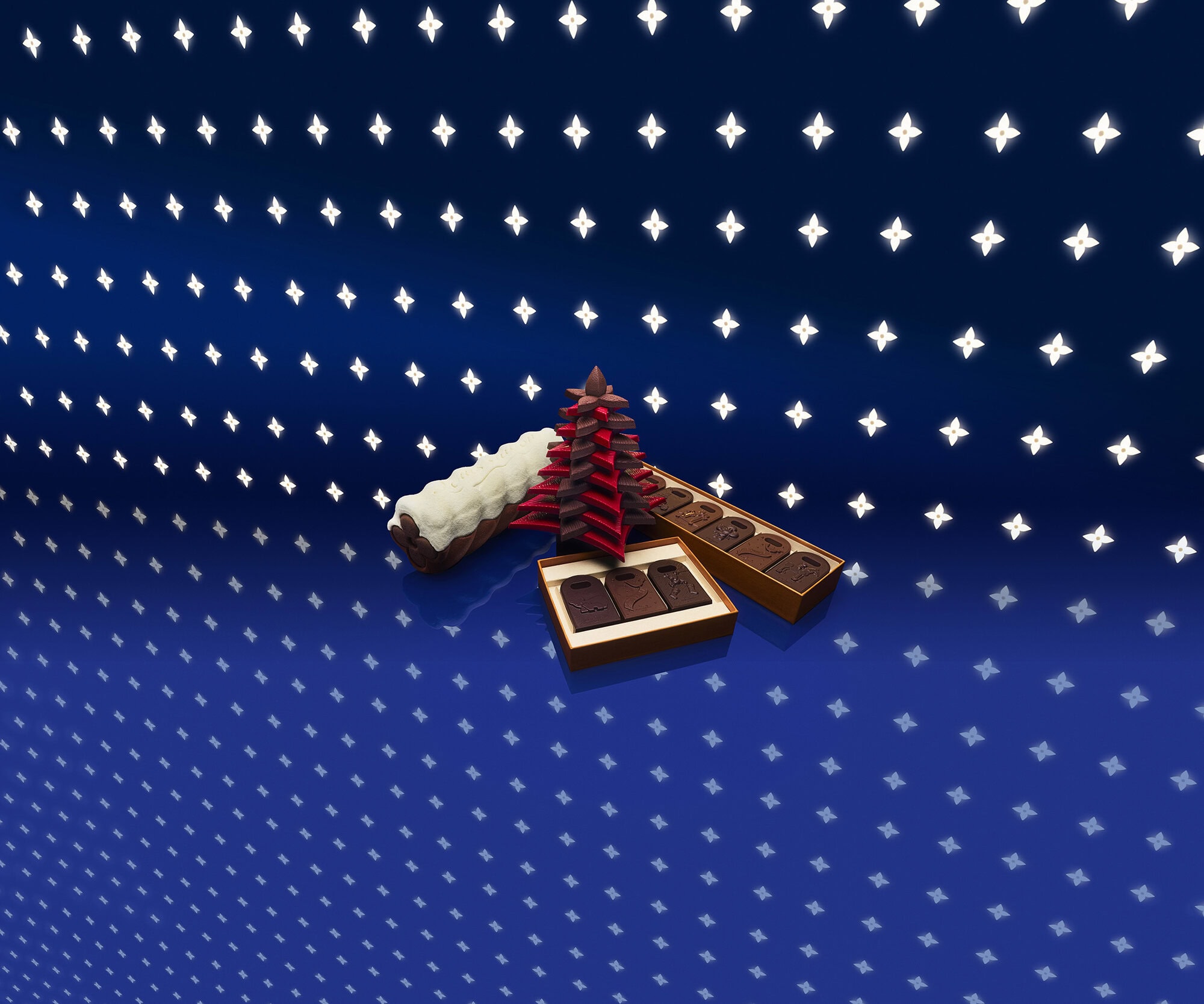 Gourmet chocolates and festive tree-shaped confections arranged on a glossy blue patterned surface for Louis Vuitton Holiday campaign.