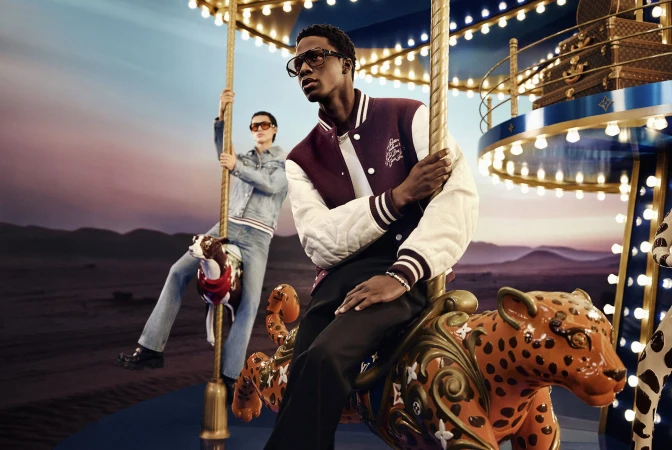 Black man wearing a burgundy varsity jacket seated on an ornate carousel animal for Louis Vuitton Holiday 2024 campaign