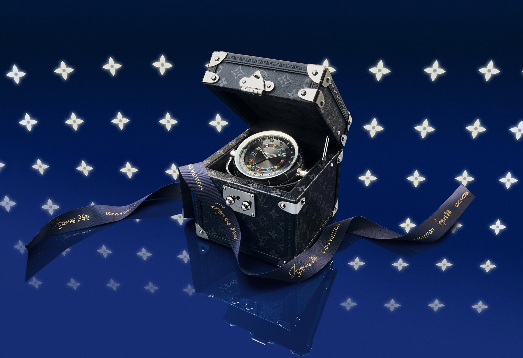 Monogram trunk watch case open with ribbon on a dark blue glossy surface against glowing star pattern background