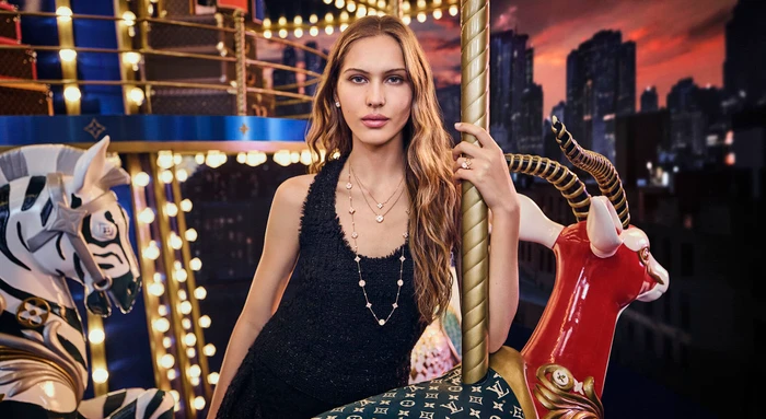 Model standing on a carousel holding a golden pole wearing layered necklaces and a black top