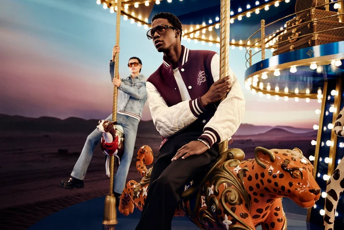 Black man wearing a burgundy varsity jacket seated on an ornate carousel animal for Louis Vuitton Holiday 2024 campaign