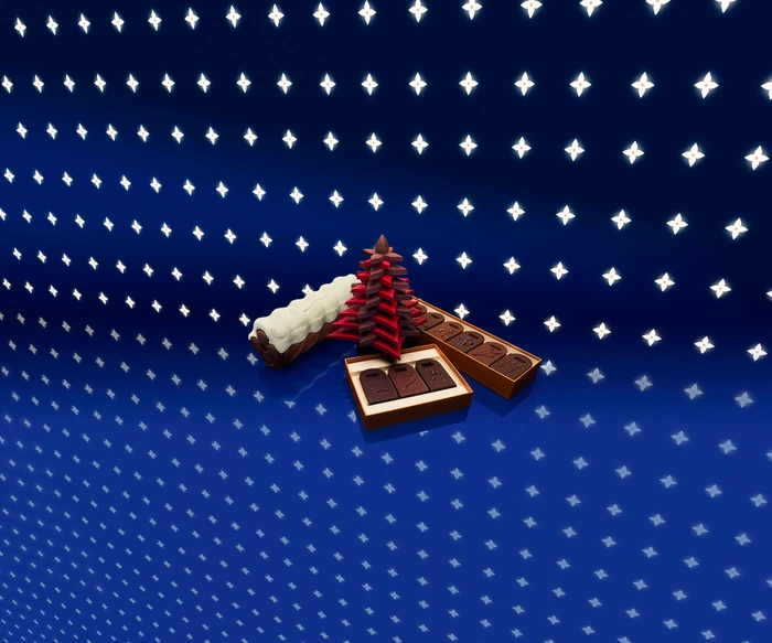 Gourmet chocolates and festive tree-shaped confections arranged on a glossy blue patterned surface for Louis Vuitton Holiday campaign.