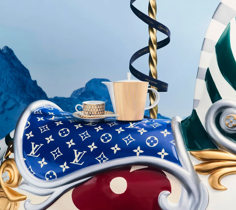 Porcelain teapot and teacup resting on a blue monogram saddle atop a decorative carousel against mountain backdrop
