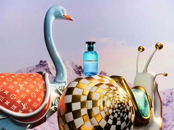 Blue perfume bottle resting on a gold and white snail sculpture next to a blue bird sculpture against a mountain landscape background