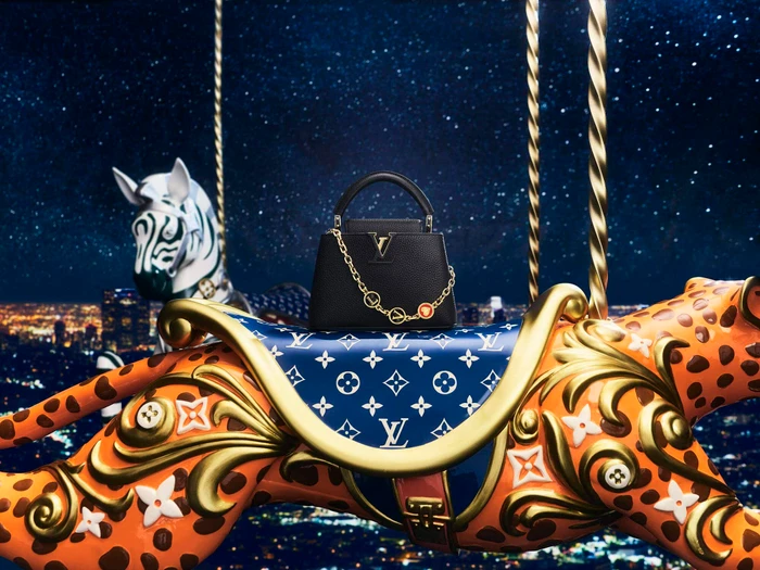Black leather handbag with gold chain resting on a carousel animal against a starry night cityscape.