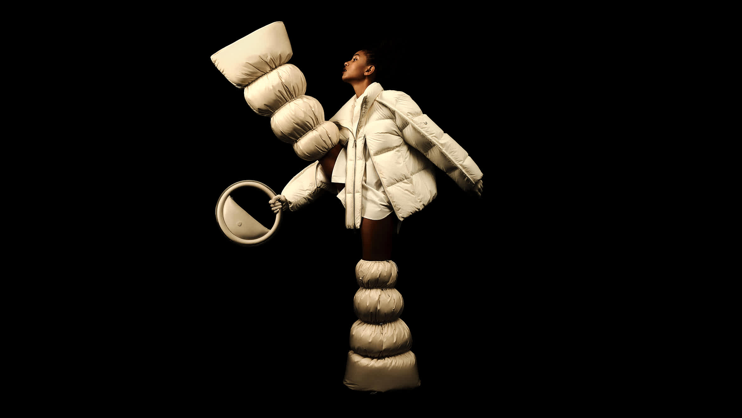 Willow Smith modelling in a puffy white jacket and oversized sculptural puffer leg pieces against a stark black background.