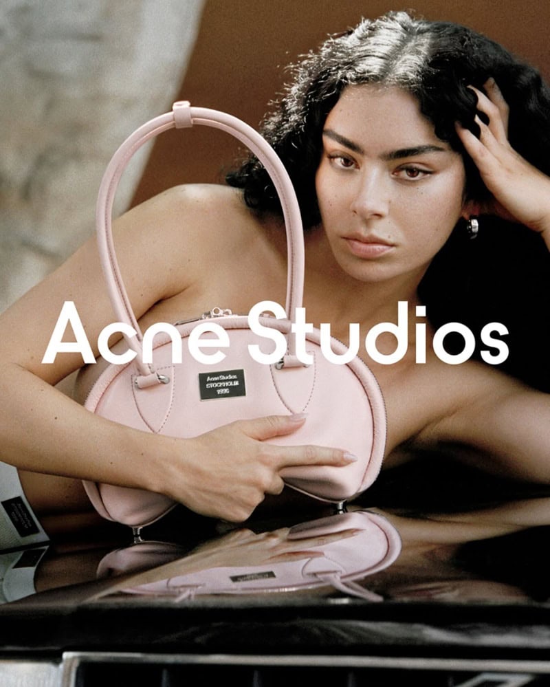 Woman holding a pink handbag against a car hood for the Acne Studios Spring 2025 ad campaign.