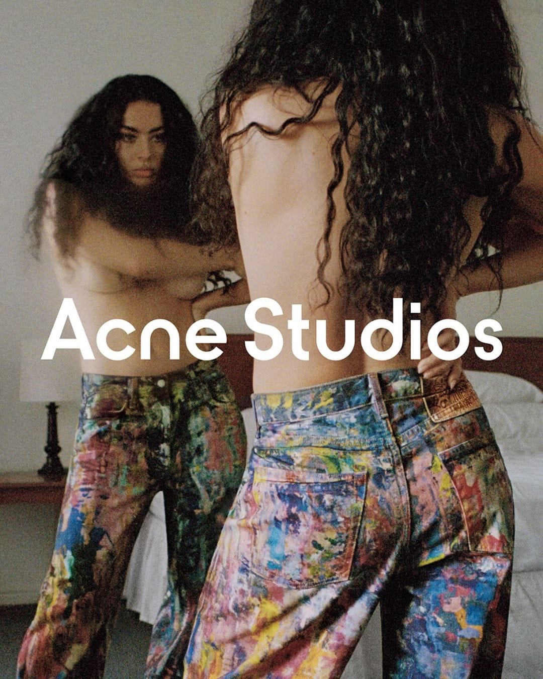 Model with long dark hair wearing colorful patterned jeans reflected in a mirror for Acne Studios campaign