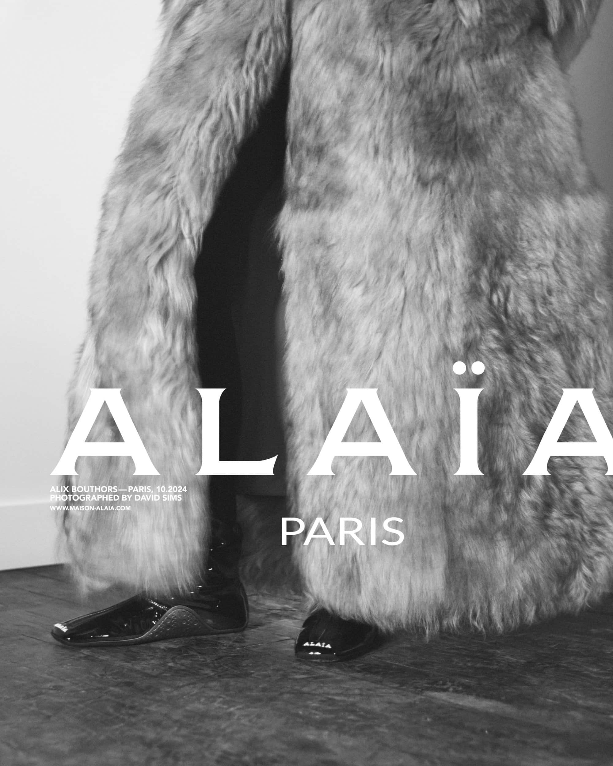Monochrome fashion campaign image featuring a person wearing a textured fur coat and dark footwear against a plain background