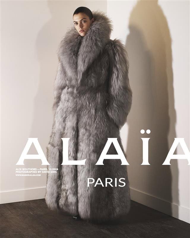 Model Alix Bouthors wearing a voluminous grey fur coat against a plain wall for Alaïa Spring 2025 campaign.