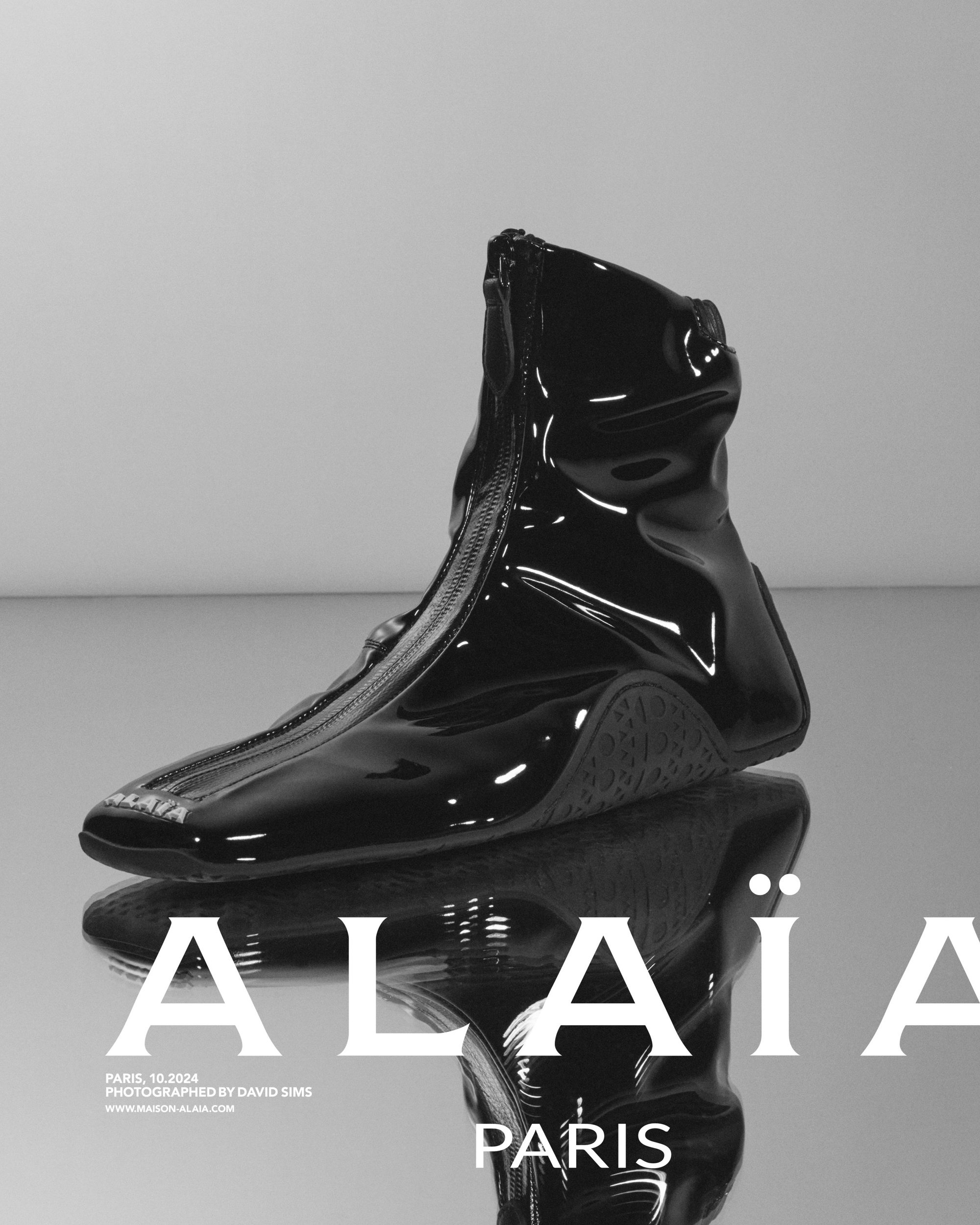 Black patent leather zippered boot with reflective sole on glossy grey background for Alaïa campaign