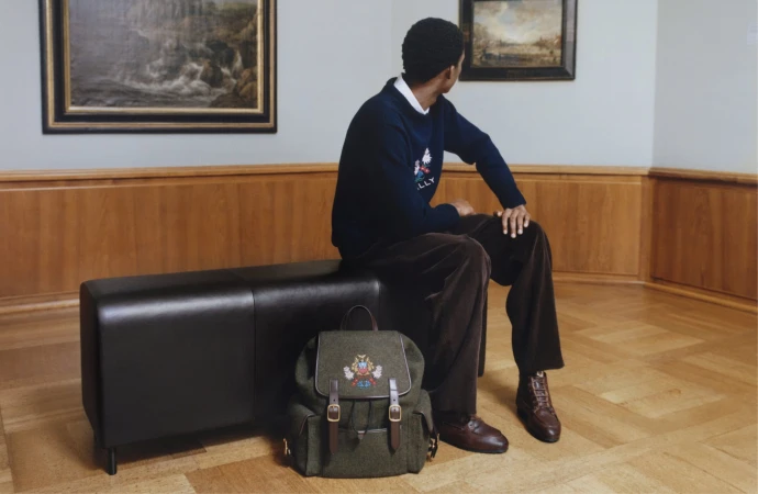 Man seated on a black leather bench in a museum gallery viewing framed landscape paintings, with an olive green backpack on the floor.