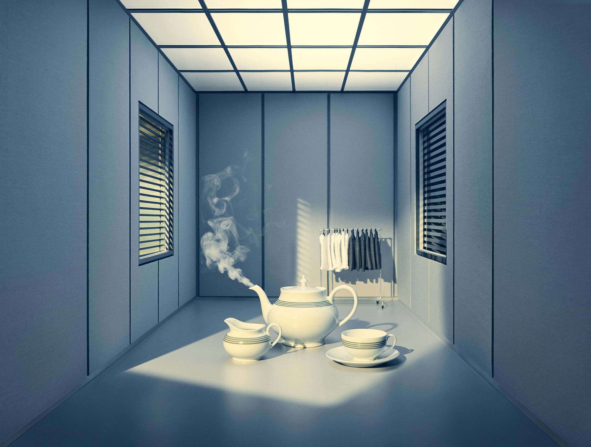 White ceramic teapot steaming with a matching creamer and cup in a gray minimalist office room with a grid-lit ceiling.