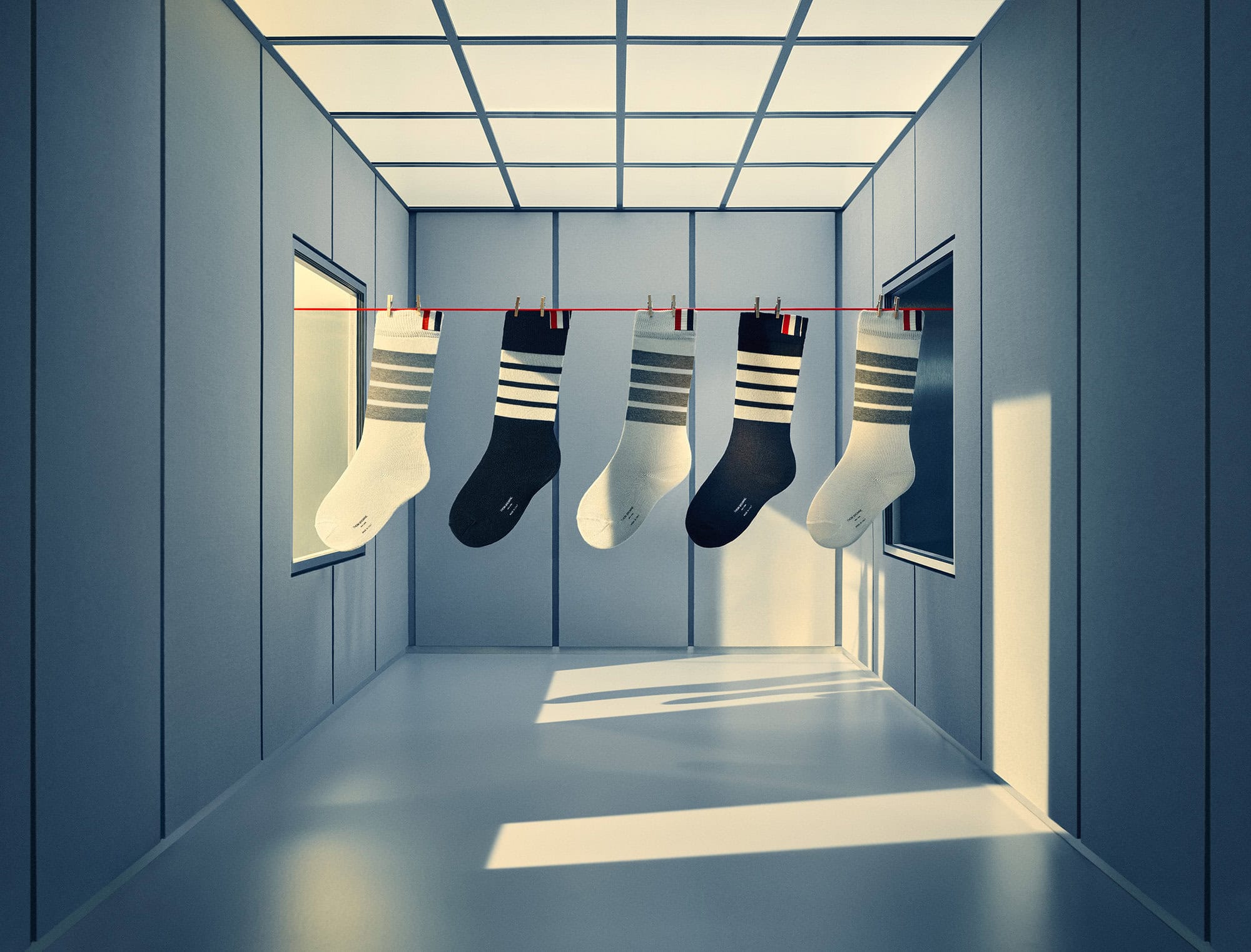 Five pairs of striped socks hanging on a red clothesline inside a grey symmetrical hallway with lit ceiling panels