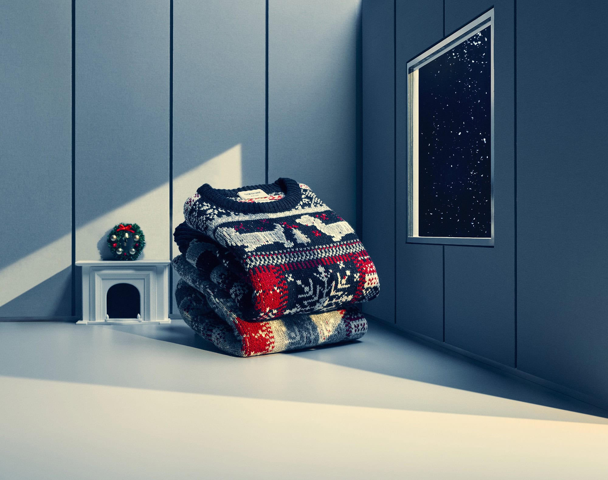 A stacked pile of patterned holiday sweaters resting on a smooth surface inside a minimalist room with a miniature fireplace.