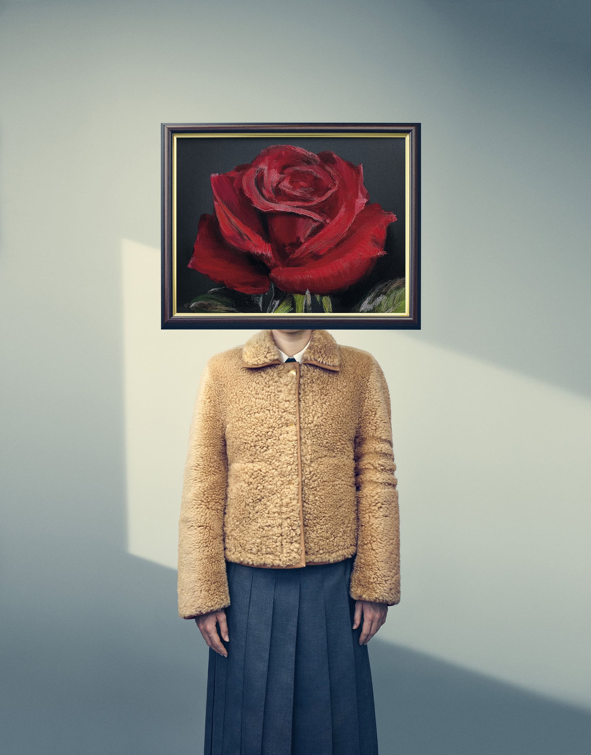 Person with a framed red rose painting in place of their head, wearing a tan shearling jacket and dark skirt.
