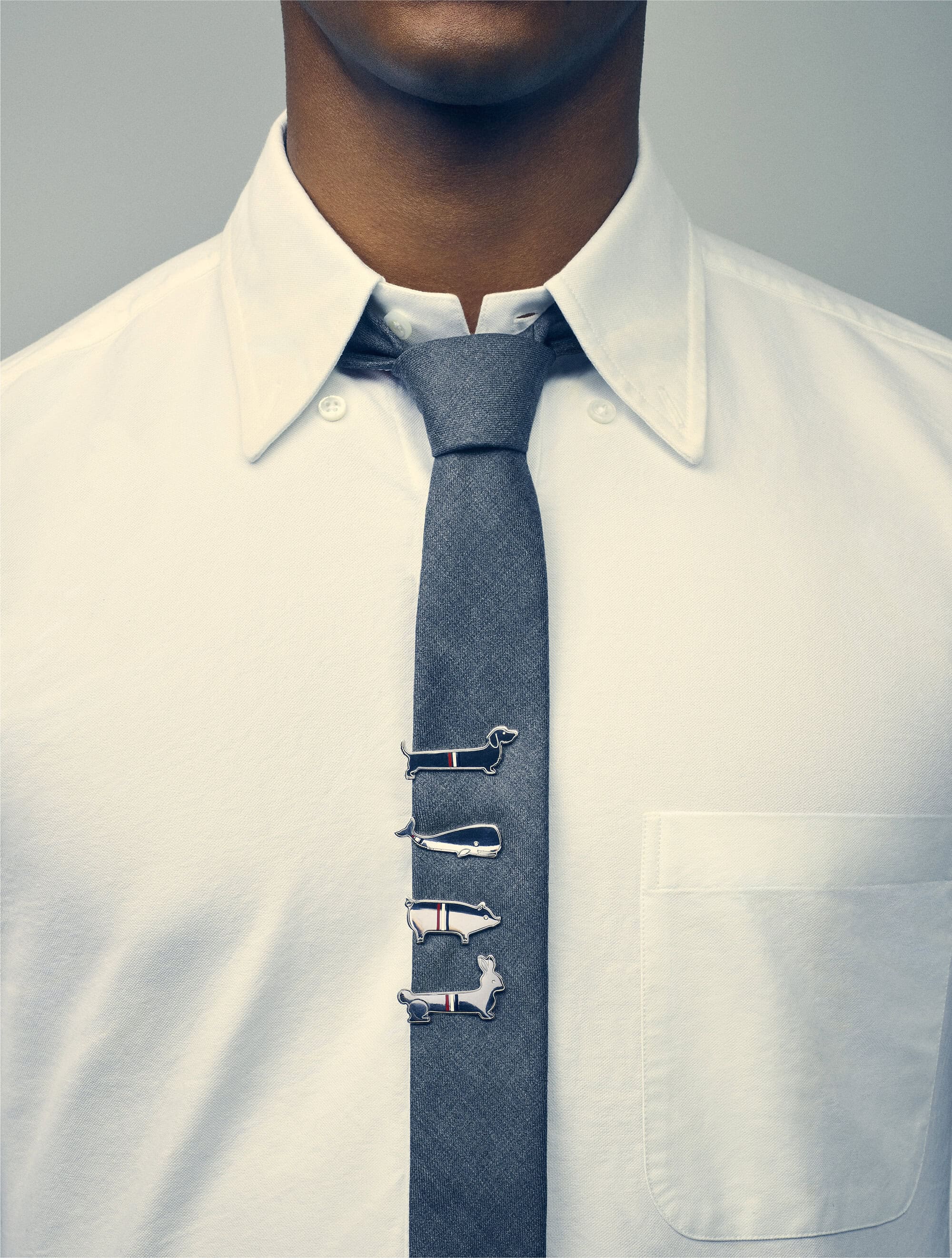 Man wearing a white dress shirt and grey tie adorned with animal-shaped tie clips against a plain light grey background.