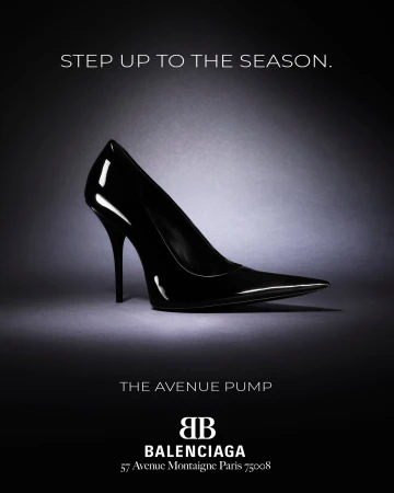 Black patent leather stiletto high heel pump set against a dark grey textured studio background with lighting highlights.