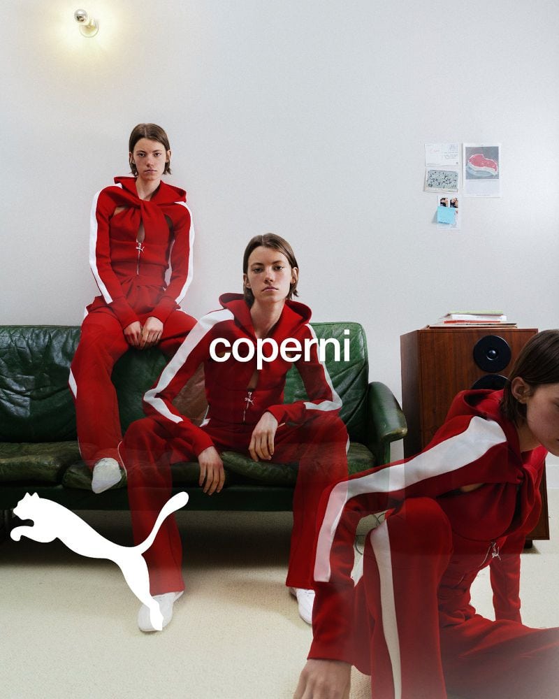 Models in matching red tracksuits with white stripes posed on and in front of a green leather sofa.
