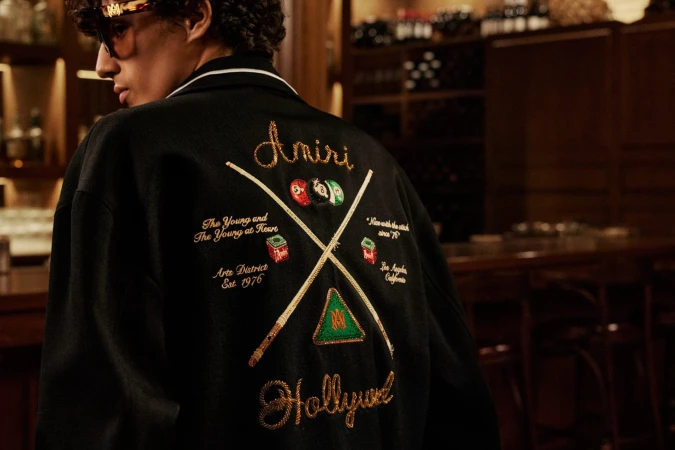 Model wearing a black jacket with detailed embroidery on the back in a dimly lit bar interior