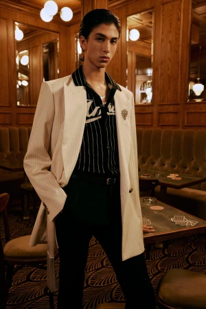 Model wearing a white pinstripe blazer and black trousers in an upscale wood-paneled interior for Amiri.