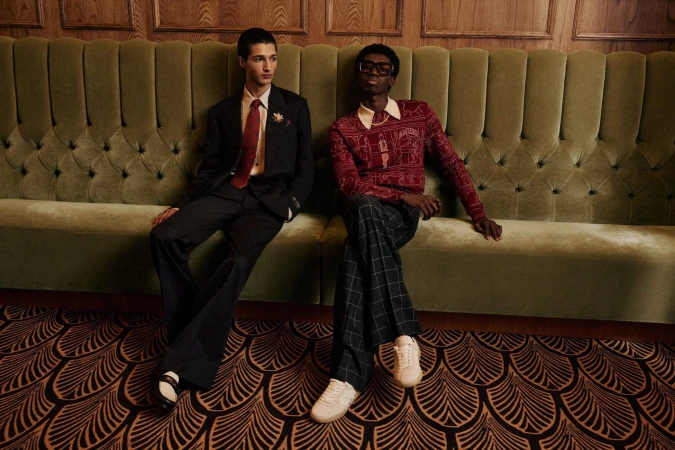 Two men seated together on a large green tufted velvet banquette in an interior setting for Amiri Pre-Spring 2025 campaign.