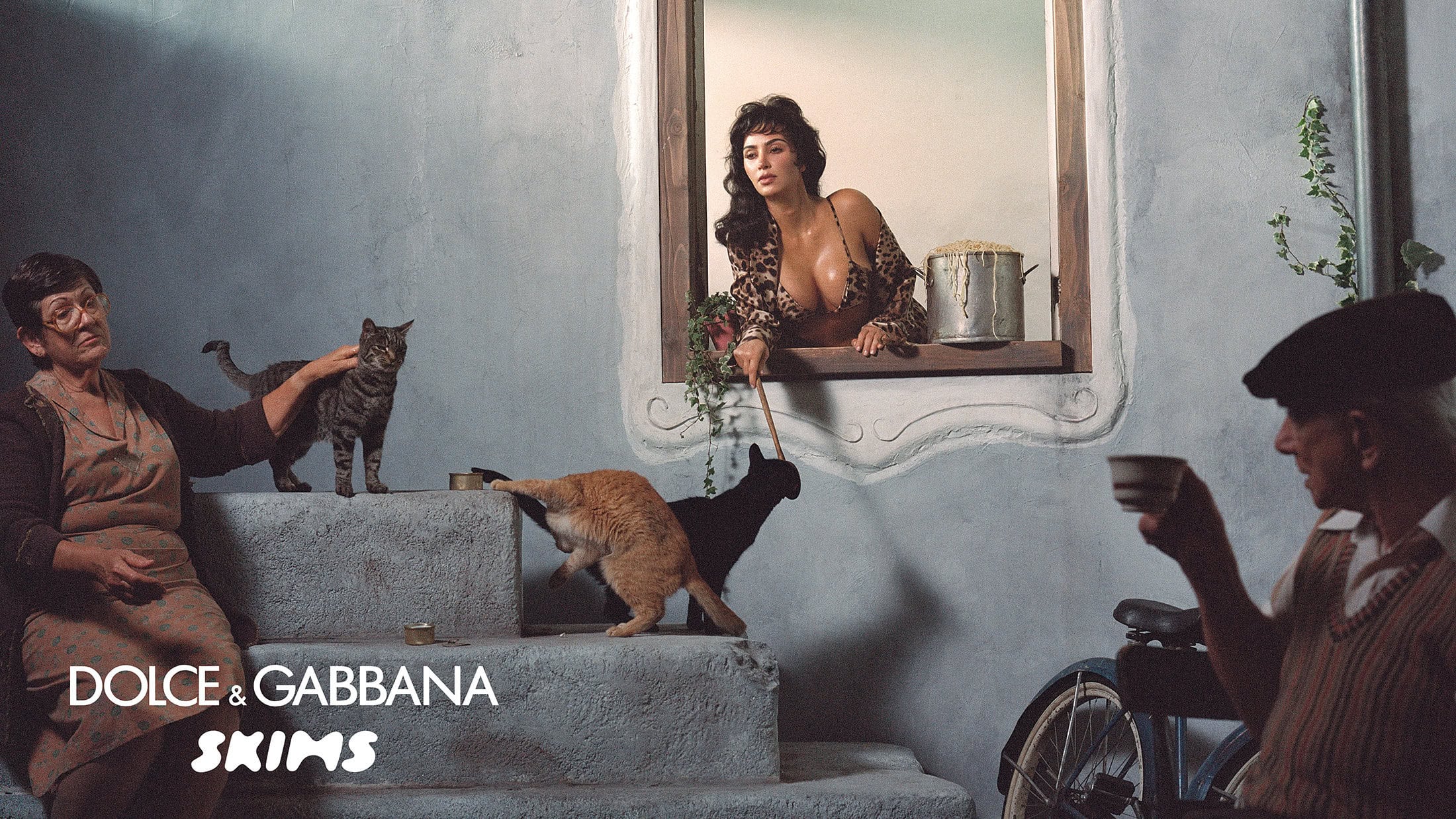 Kim Kardashian leaning out a rustic window overlooking an Italian street scene with cats and local residents.