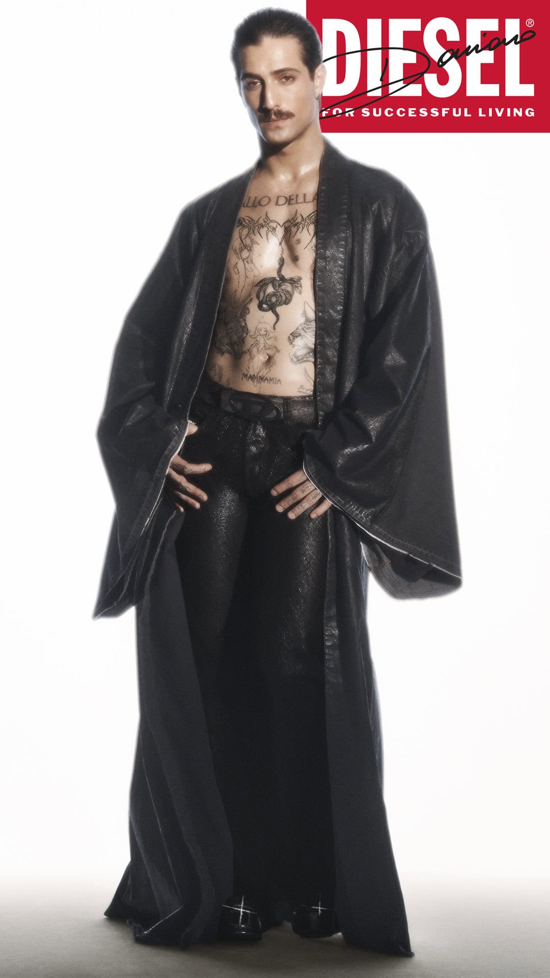 Model Damiano David wearing a long dark coat and matching trousers against a bright white background for Diesel