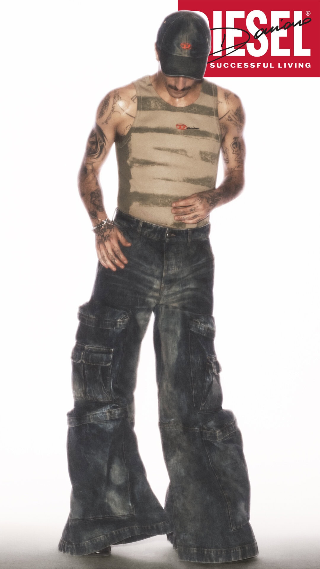 Man wearing a striped tank top, dark baggy cargo pants, and a baseball cap against a white background.