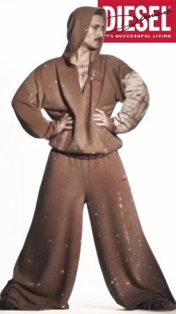 Damiano David in a sparkly brown hoodie and wide trousers posing against white