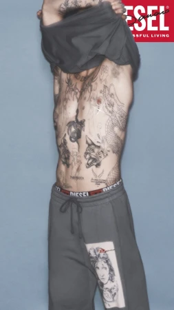 Damiano David taking off a dark grey top against a grey backdrop for Diesel Fall 2024 ad campaign